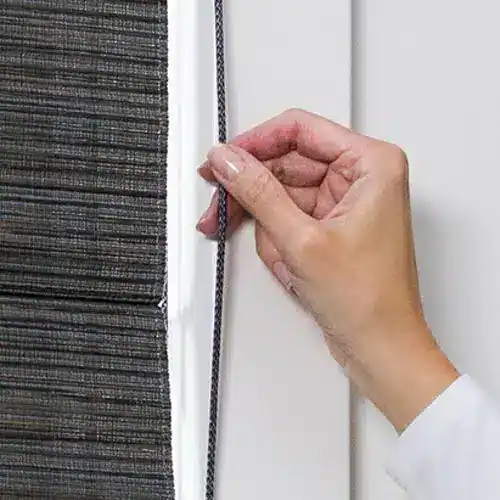 Hand using the EasyRise cord loop on Hunter Douglas Alustra Woven Textures Roman Shades