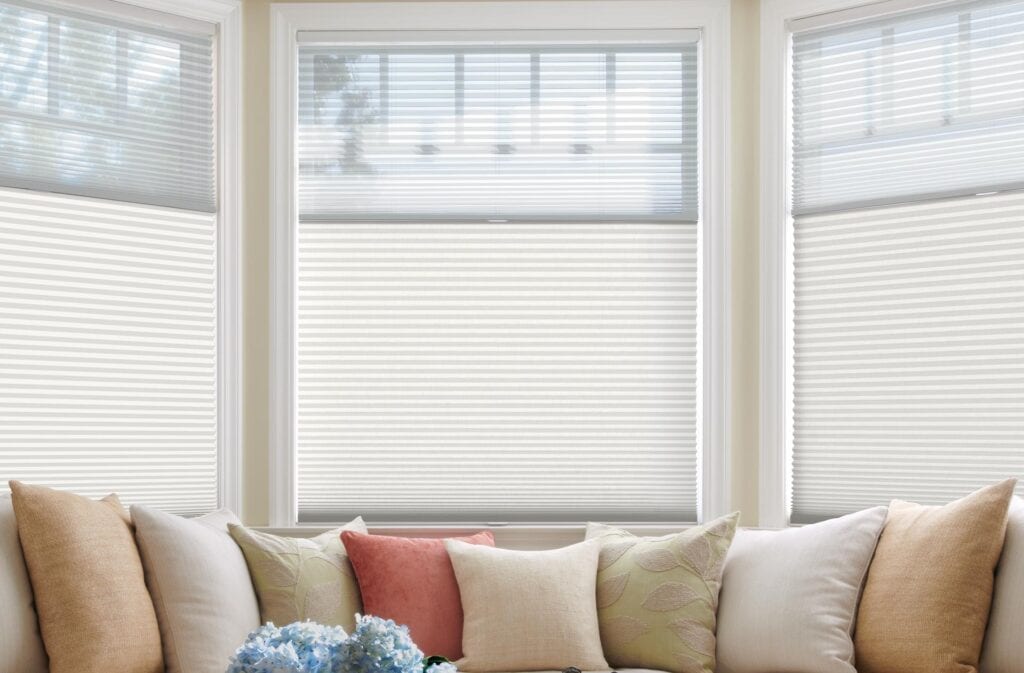 Bright living room with white window blinds, beige sofa, and assorted throw pillows with floral and textured designs.