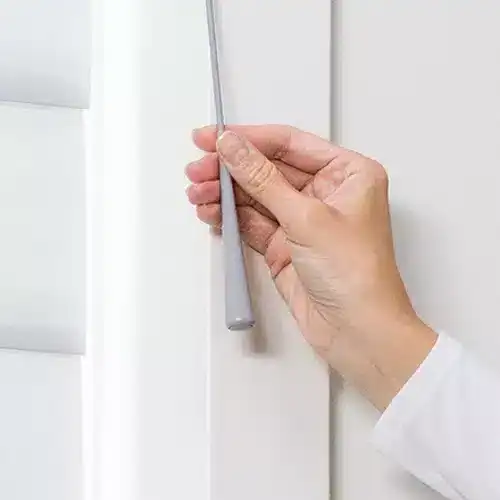 Close-up of hand using a cleaning tool on a white window frame.
